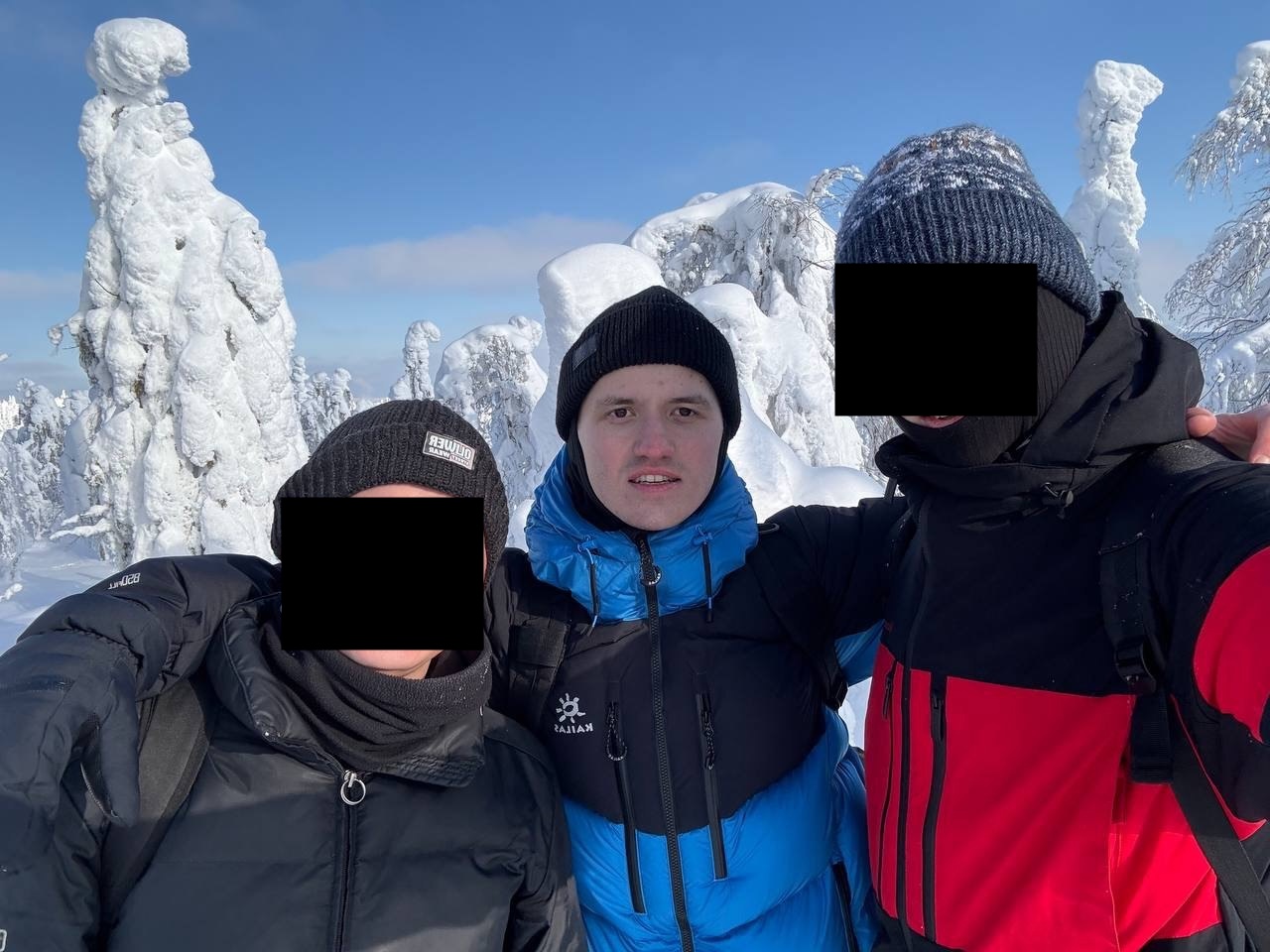 Женя в синей куртке между двумя друзьями на фоне заснеженных деревьев; лица друзей закрыты чёрными прямоугольниками
